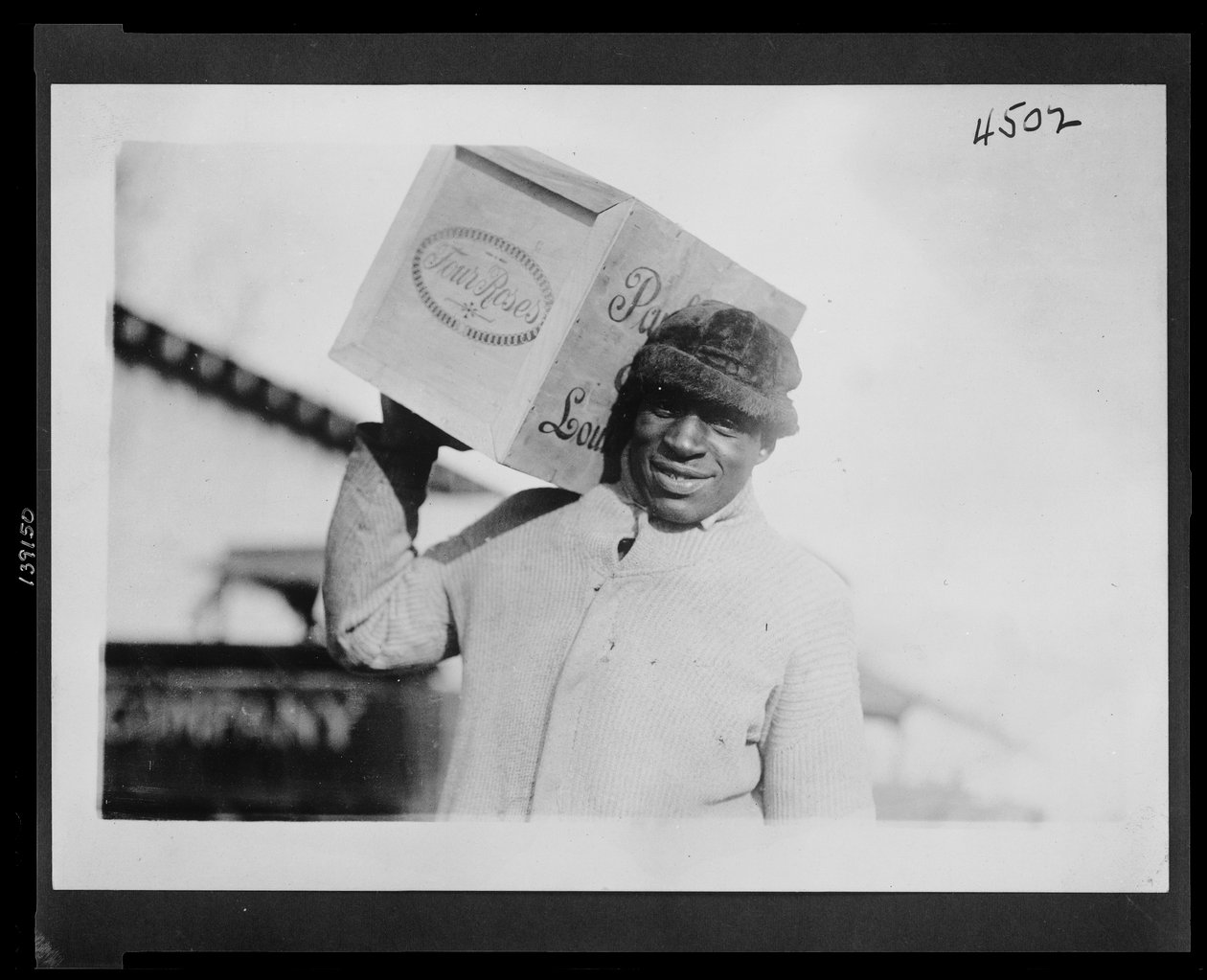 Afroameričan nesoucí na rameni bednu whisky „Four Roses“, možná zabavenou americkým úřadem Internal Revenue Bureau od American Photographer