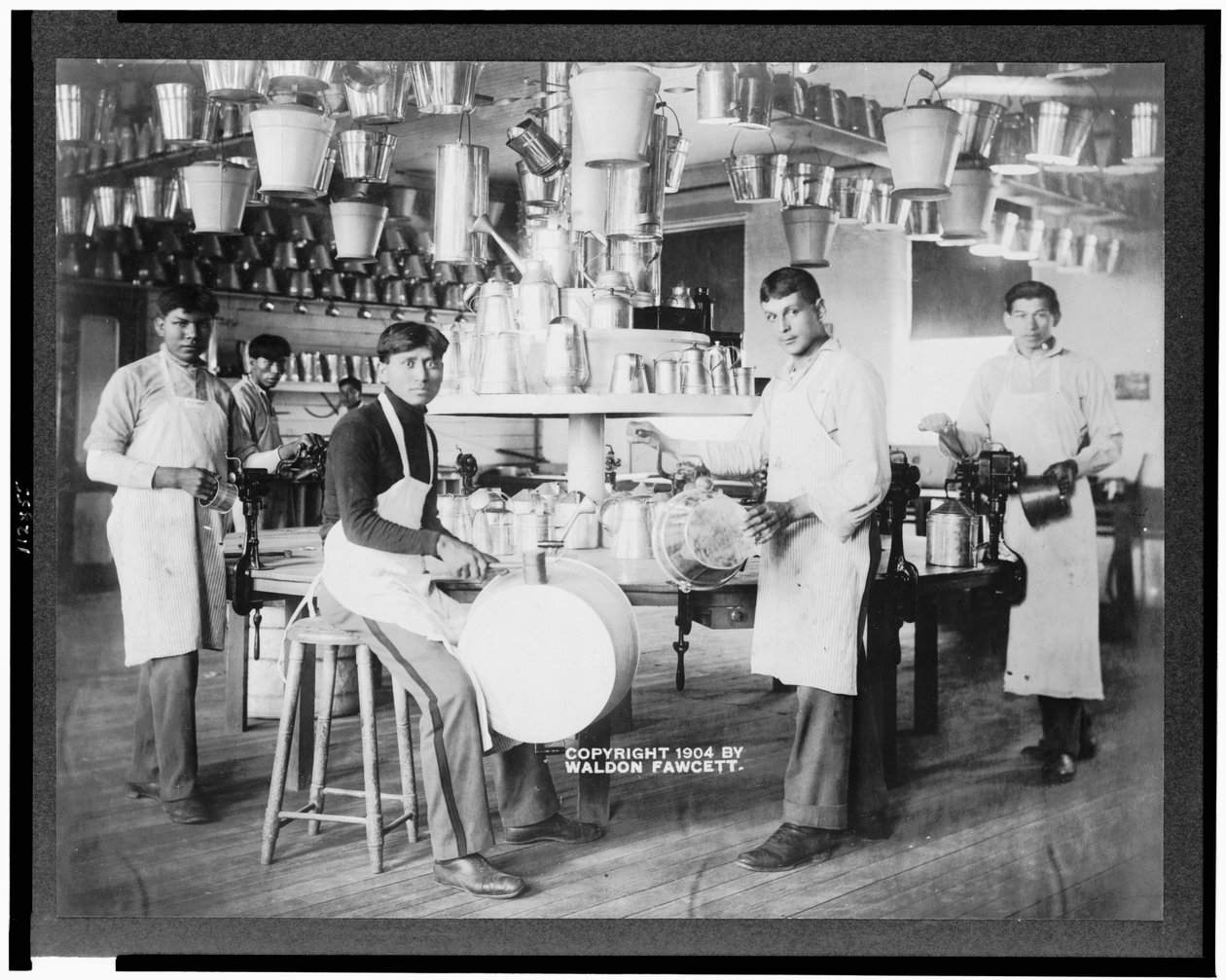 Mladí indiáni v kovoobráběcí dílně s kbelíky, umyvadly, konvemi a dalšími kovovými předměty, Carlisle Indian School, Pennsylvania, kolem roku 1904 (černobílá fotografie) od American Photographer