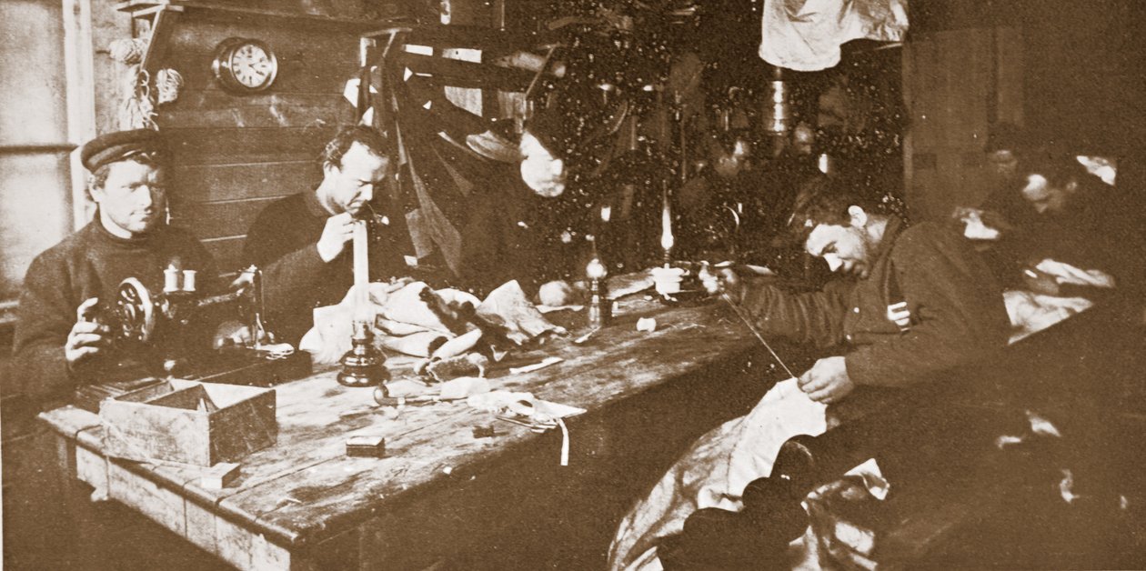V Chatě uprostřed zimy se muži zabývali šitím kožešin na oděvy pro jarní sáňkování, hospoda. Londýn 1907 (černobílá fotografie) od Anthony Fiala