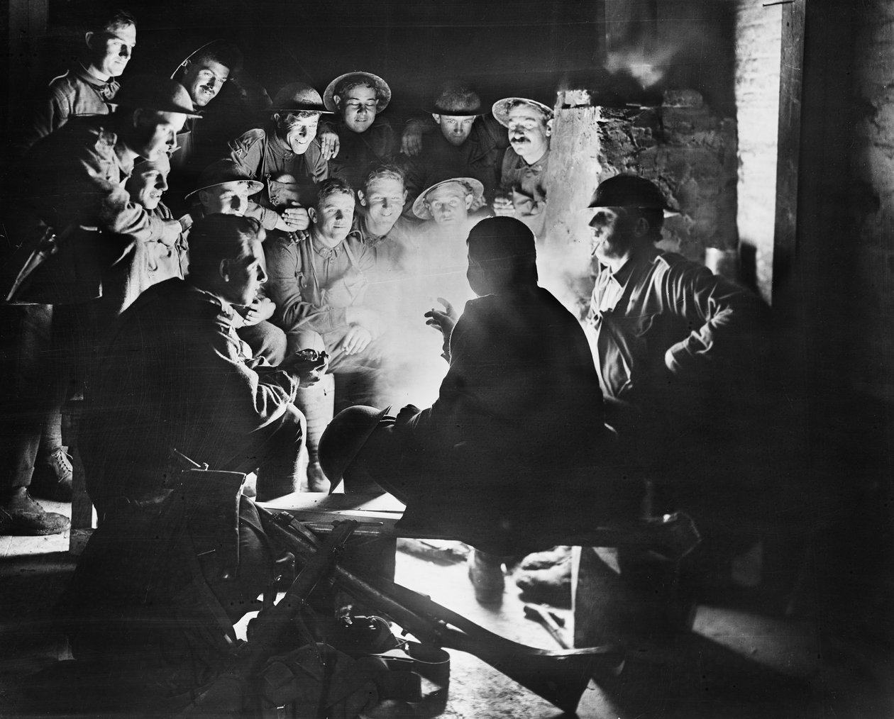 Členové 1. australské lehké příkopové minometné baterie, 1. australská divize poslouchají nejnovější zprávy od jednoho ze svých kamarádů kolem požáru v kopané v Ypres, 28. října 1917 (bw pho od Australian Photographer