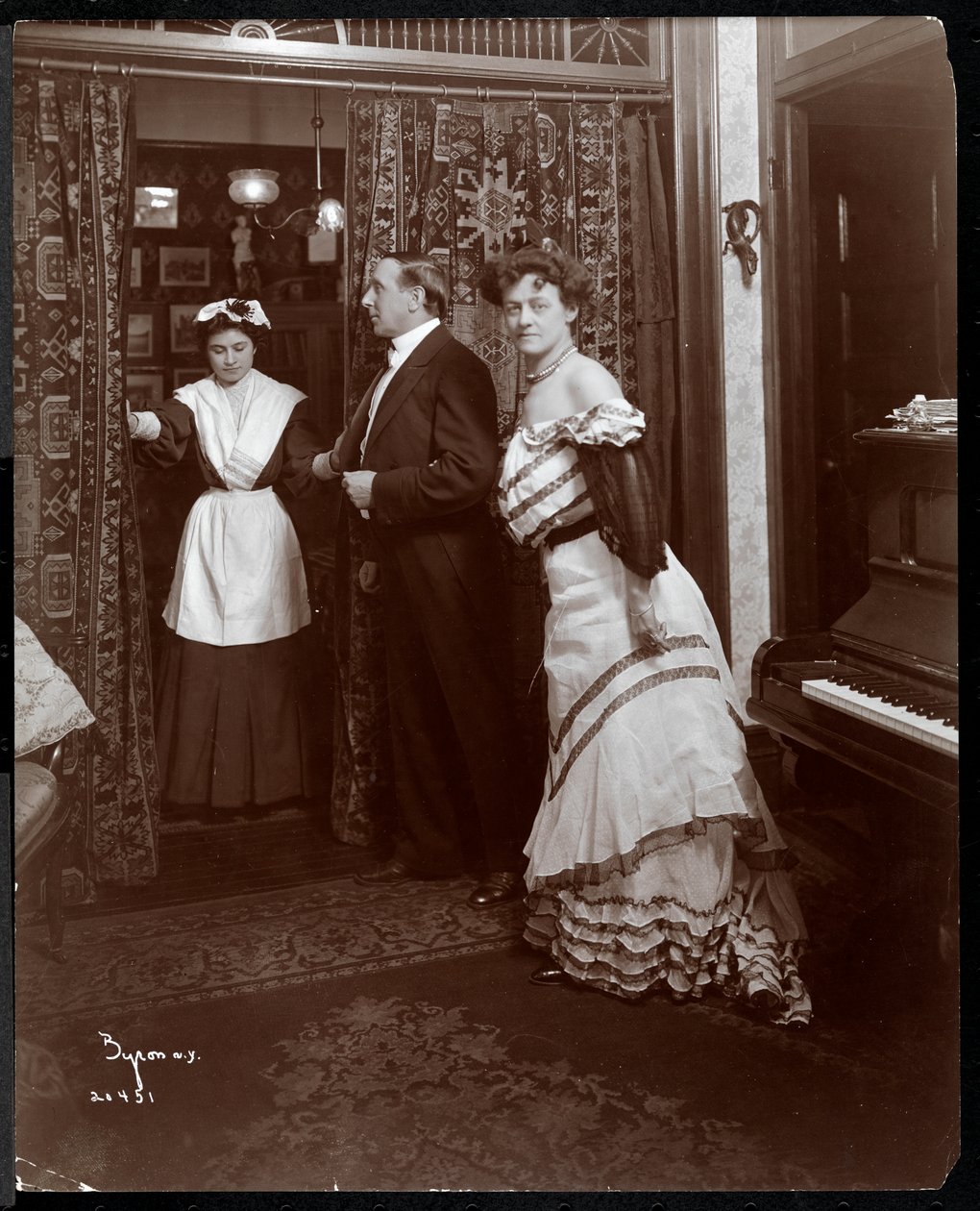 Formálně oblečení muž a žena a zřejmě služka v místnosti s klavírem, 1905 (stříbrný želatinový tisk) od Byron Company
