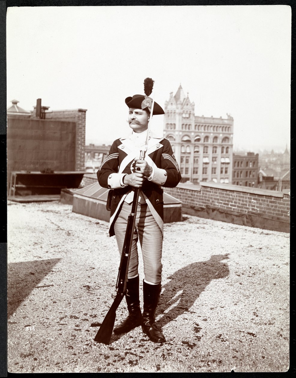 Muž na střeše oblečený v tradiční vojenské uniformě, držící pušku, 1895 (stříbrný želatinový tisk) od Byron Company
