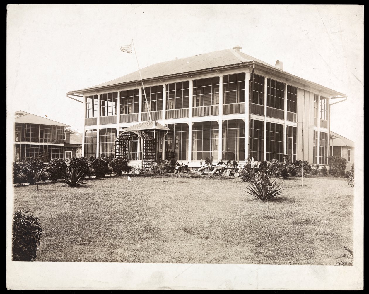 Dvoupatrový dům obklopený verandami s vlající americkou vlajkou; v Panamě při stavbě kanálu, 1912 (stříbrný želatinový tisk) od Byron Company