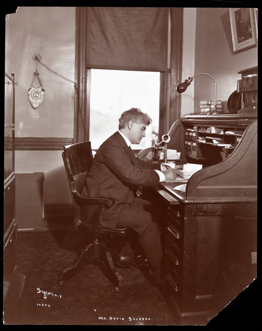 David Belasco píše u stolu v kancelářích svého divadla, 1902 (stříbrný želatinový tisk) od Byron Company