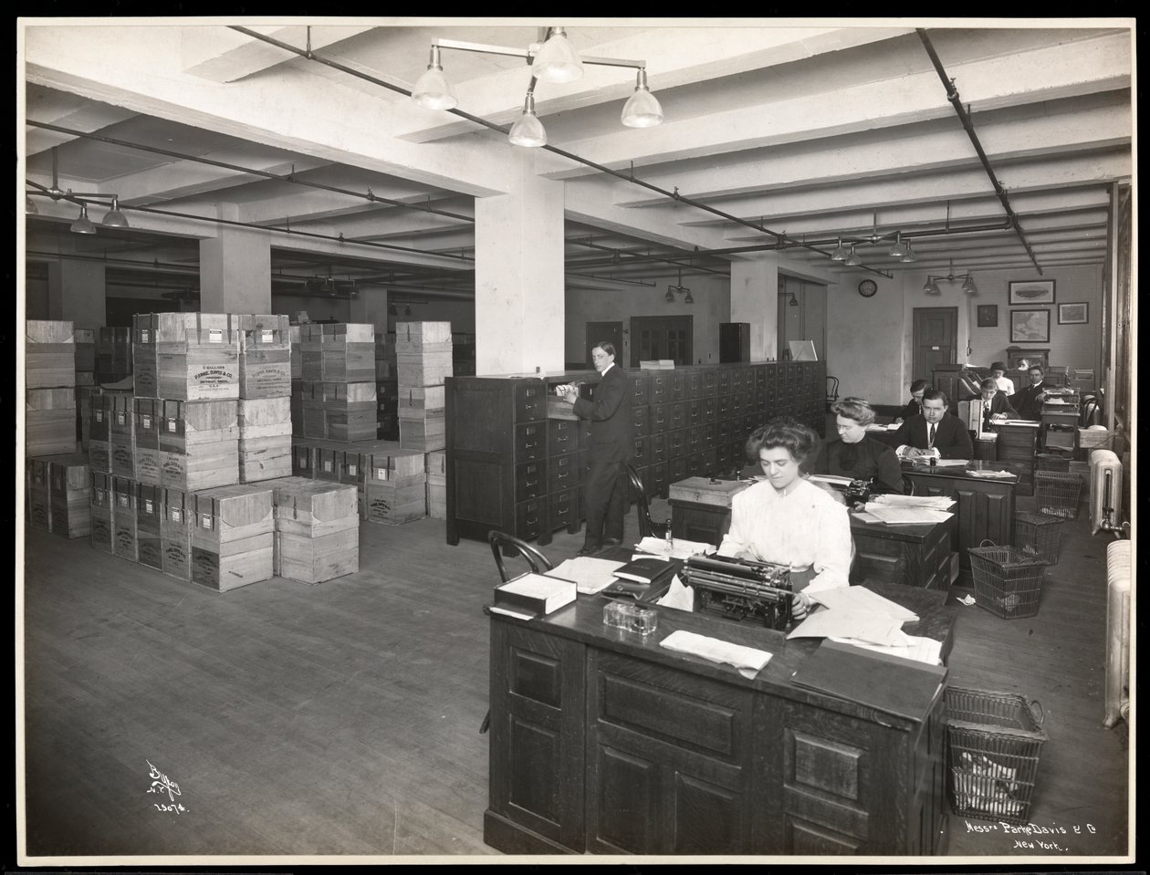 Pohled na muže a ženy u přepážek v něčem, co vypadá jako expediční místnost v Parke, Davis und Co., chemici, Hudson und Vestry Streets, New York, 1910 (potisk stříbrnou želatinou) od Byron Company