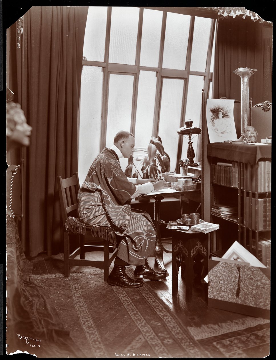 Will R. Barnes v róbě, sedící u stolu ve svém ateliéru, 1903 (stříbrný želatinový tisk) od Byron Company