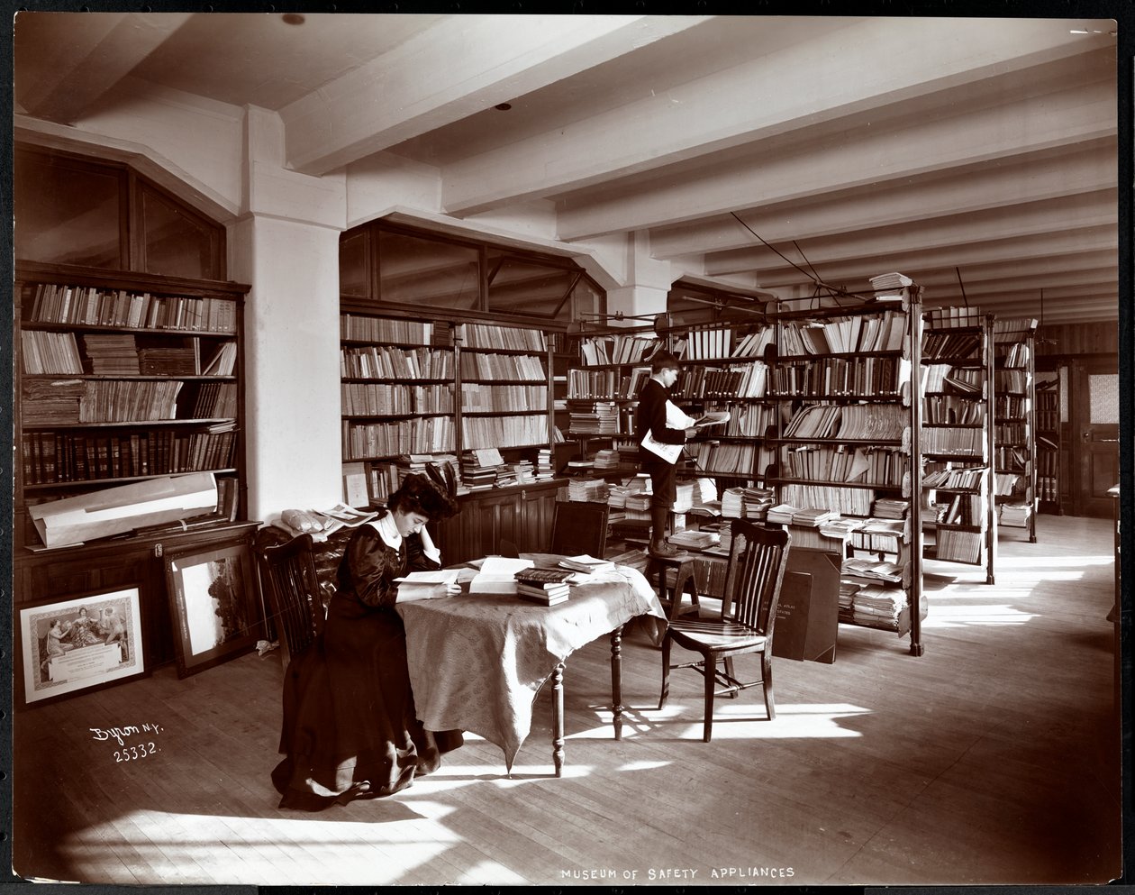 Žena a mladý muž v knihovně Muzea bezpečnostních zařízení Amerického institutu sociálních služeb, New York, 1907 (stříbrný želatinový tisk) od Byron Company