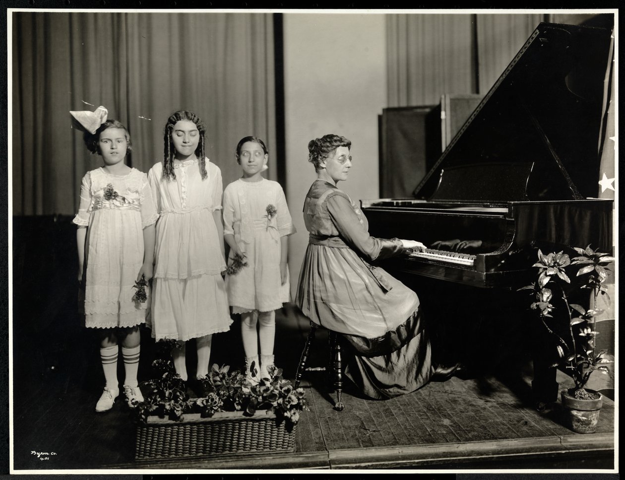 Žena hrající na klavír, zatímco tři dívky zpívají v New York Association for the Blind, 111 East 59th Street, New York, kolem roku 1917 (potisk stříbrné želatiny) od Byron Company