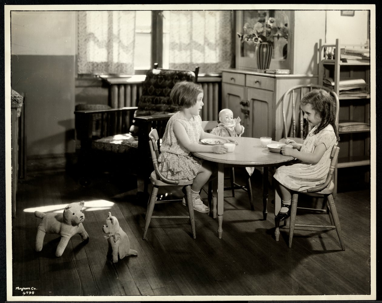Dvě slepé zrakově postižené dívky jedí u malého stolku s panenkou v New York Association for the Blind, 111 East 59th Street, New York, 1933 (potisk stříbrnou želatinou) od Byron Company