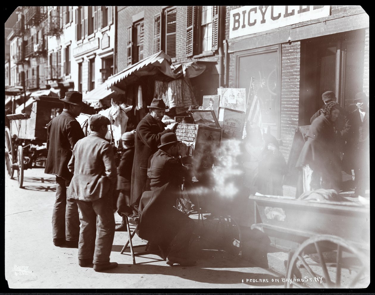 Pohled na pouliční prodavače, včetně jednoho, který ukazuje fotografické pohledy na exotická místa ve zobrazovacím poli, na Bayard Street, New York, 1898 (stříbrný želatinový tisk) od Byron Company