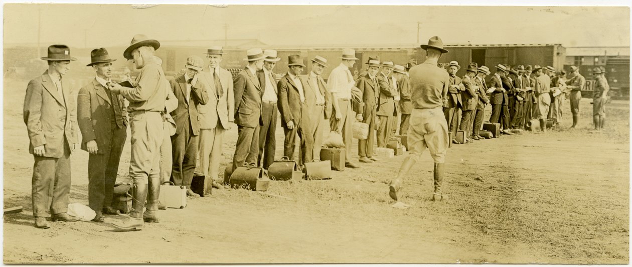 Horizontální, sépiová fotografie zobrazující skupinu mužů v civilu, z nichž mnozí mají zavazadla, stojící v řadě. Vojáci v uniformách kráčejí po linii a hovoří s muži jednotlivě. V ba jsou vidět koleje Raildroad a vlakové vozy od Carl Michel
