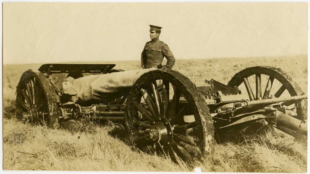 Vodorovná sépiová fotografie zachycující muže v uniformě stojícího vedle dělostřeleckého děla na kolečkách na otevřeném poli. od Carl Michel
