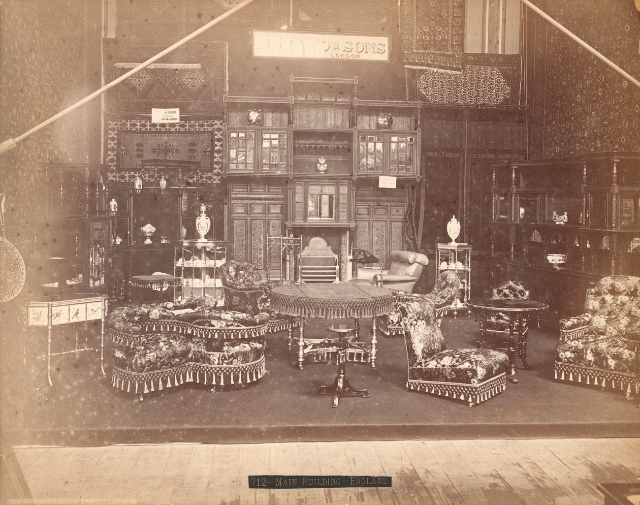 Expozice S. Howard & Sons -- hlavní budova, sbírka nábytku, včetně čalouněných židlí, stolů, krbu, skříní a polic. Na stěnách jsou koberce a na stolech a poličkách vázy od Centennial Photographic Co.