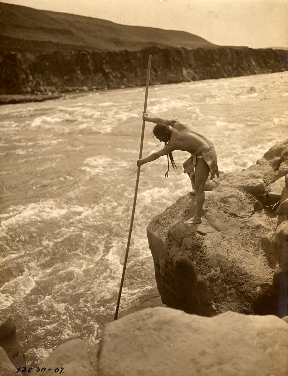 Indián Tlakluit stojící na skále a lovící ryby s namáčecí sítí, asi 1910 (čb fotografie) od Edward Sheriff Curtis