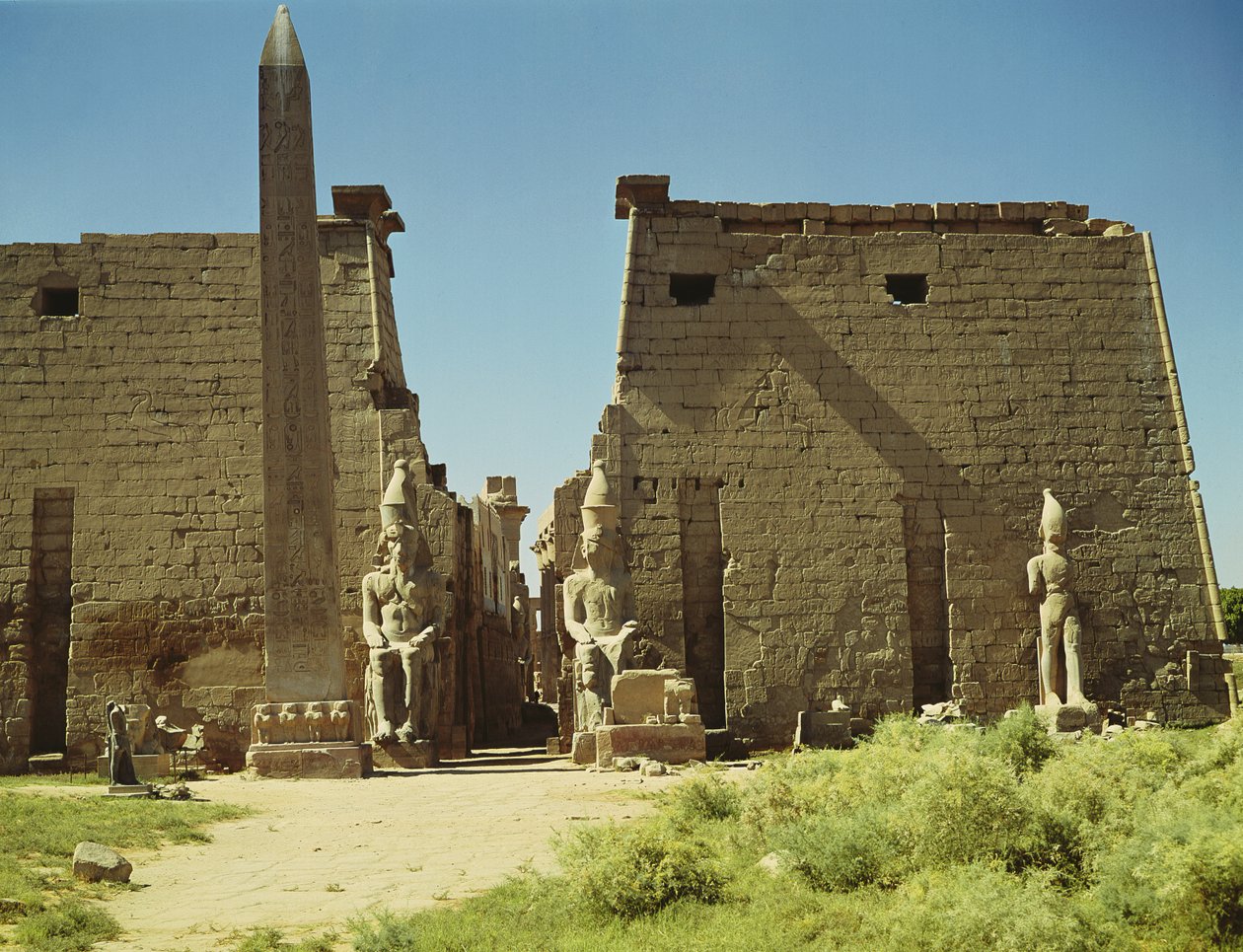 Fasáda a první pylon se dvěma sedícími sochami Ramesse II a zbývajícím obeliskem od Egyptian 19th Dynasty