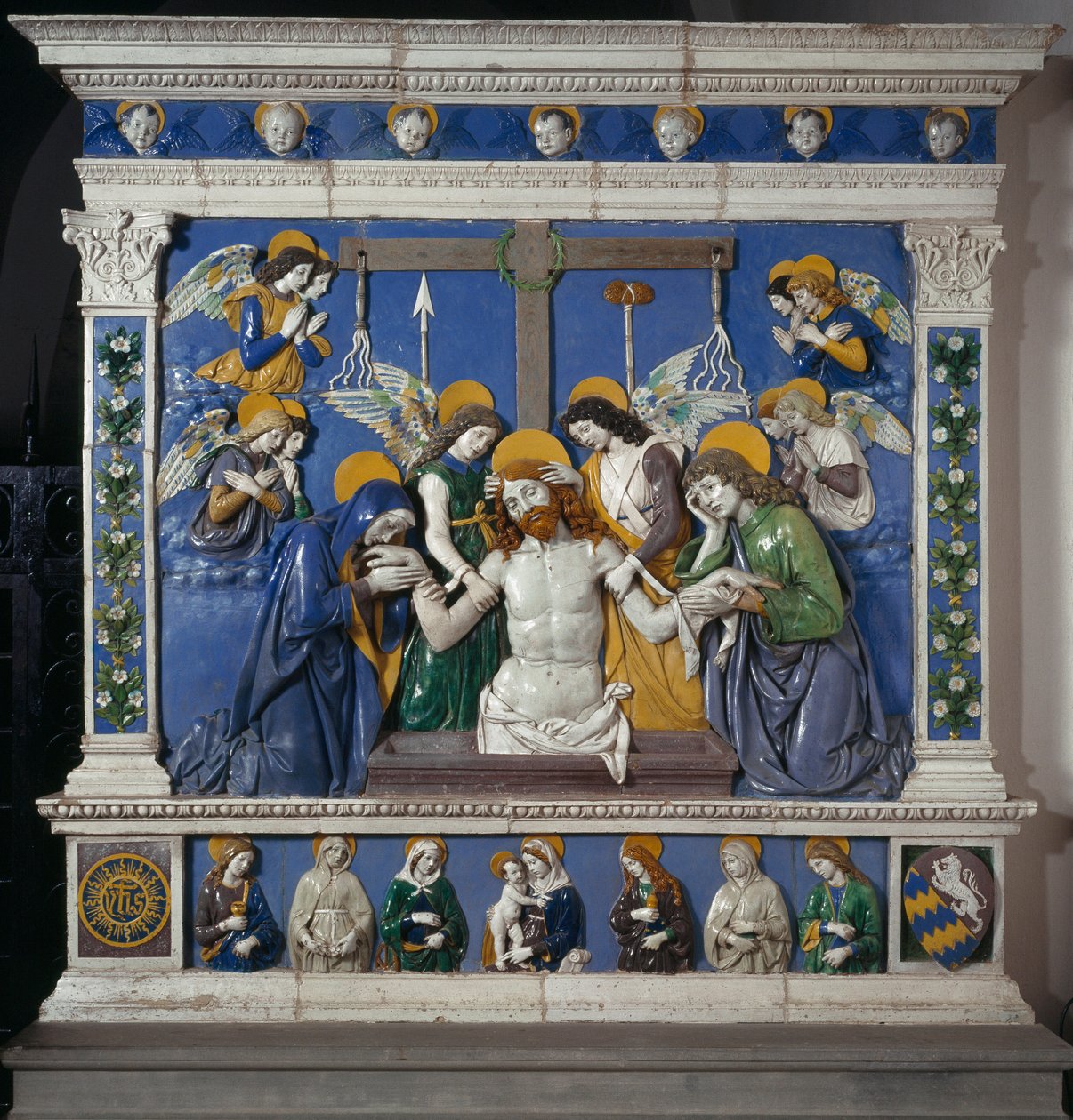 Uložení Ježíše do Božího hrobu s Pannou a svatým Janem Evangelistou Znázornění symbolů umučení: biče, trnová koruna a houba namočená v octě (posca). Vysoce reliéfní keramika od Giovanni della Robbia (1469-1529) kolem 14. od Giovanni della Robbia