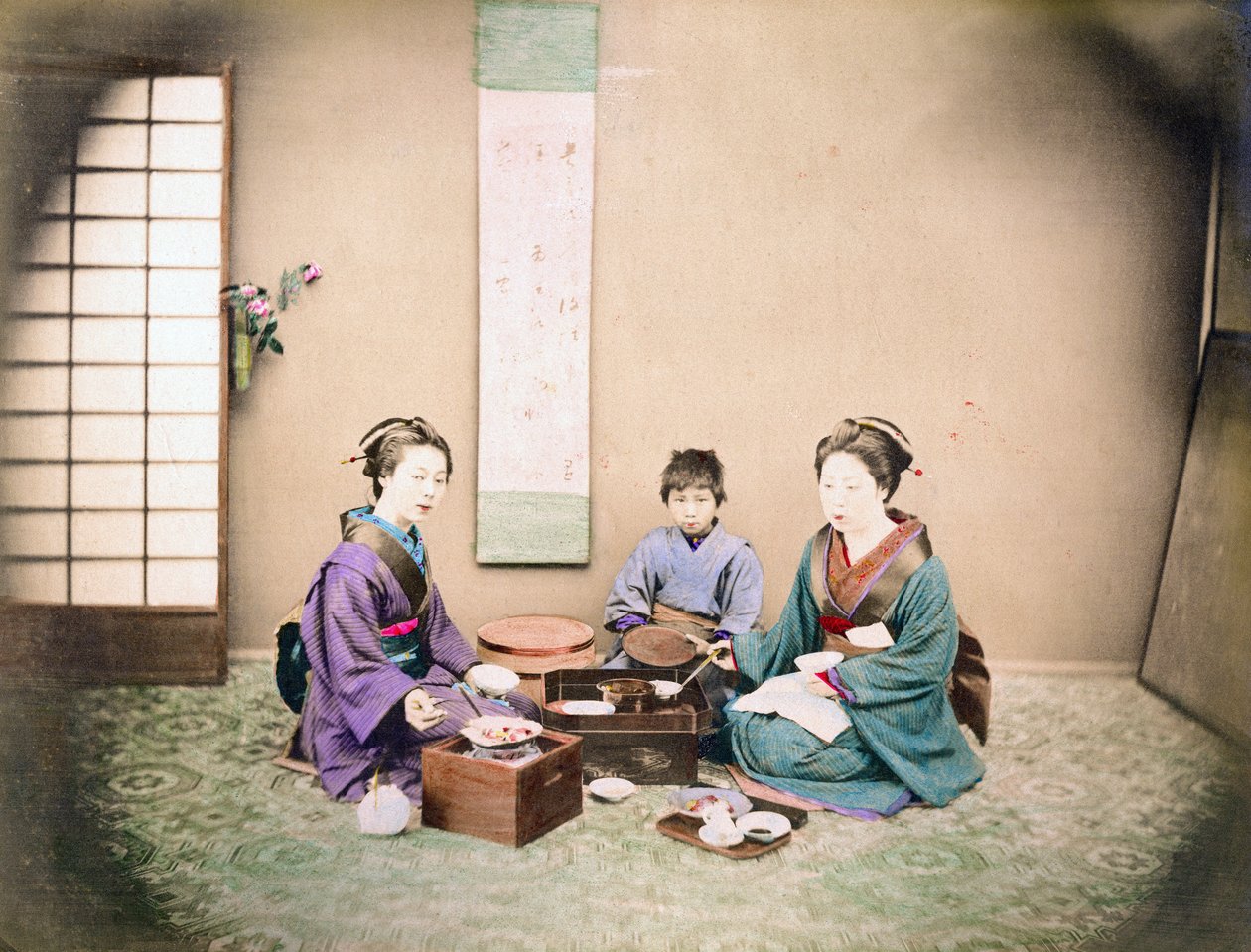 Dvě ženy a dítě obědvají, sedí na podložce, kolem roku 1890 (ručně kolorovaná fotografie) od Japanese Photographer