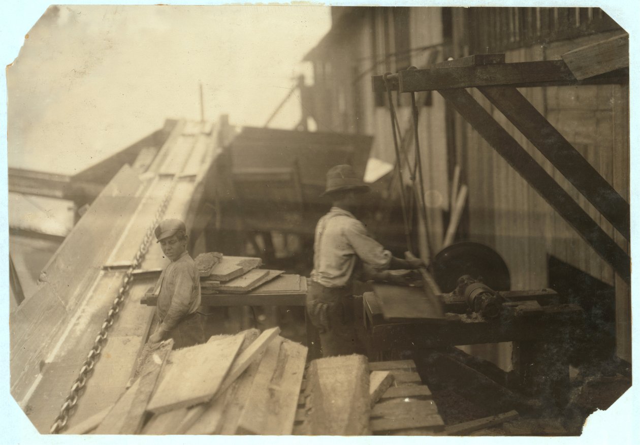 Charlie McBride ve věku 12 let odebírá dřevo ze skluzu po dobu 10 hodin ve společnosti Miller und Vidor Lumber Company, Beaumont, Texas, za což vydělává 50 centů, zatímco druhý chlapec je piluje na nestřežené kotoučové pile, 191 od Lewis Wickes Hine