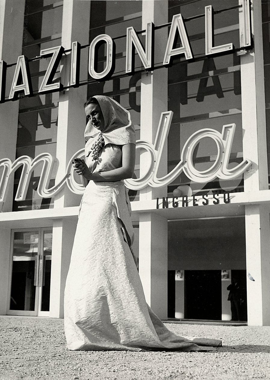 Model ve svatebních šatech vytvořený couture house "Lamma". Pro artikl je charakteristická čelenka mnišského stylu, přidržovaná u krku křiklavým špendlíkem v podobě hroznu. (černobílá fotografie) od Luis Bogino