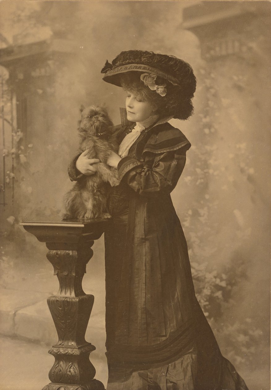 [Sarah Bernhardtová stojí v ateliéru a drží malého černého psa na zdobeném vyřezávaném dřevěném podstavci] od Theodore C. Marceau