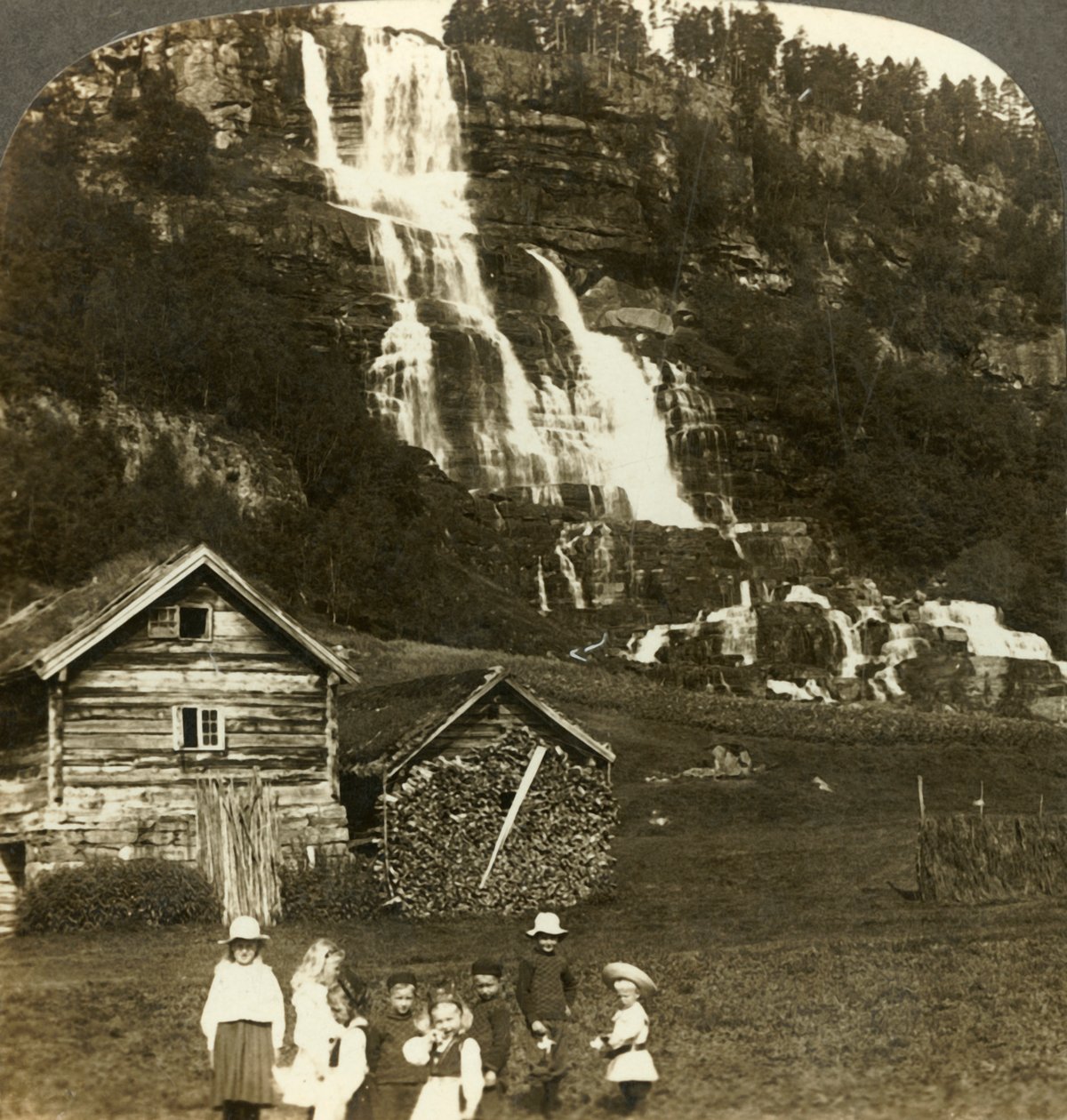 Děti si hrají na farmářském poli s terasovitým vodopádem Tvinde, Vossevangen, Norsko, c1905. od Unbekannt