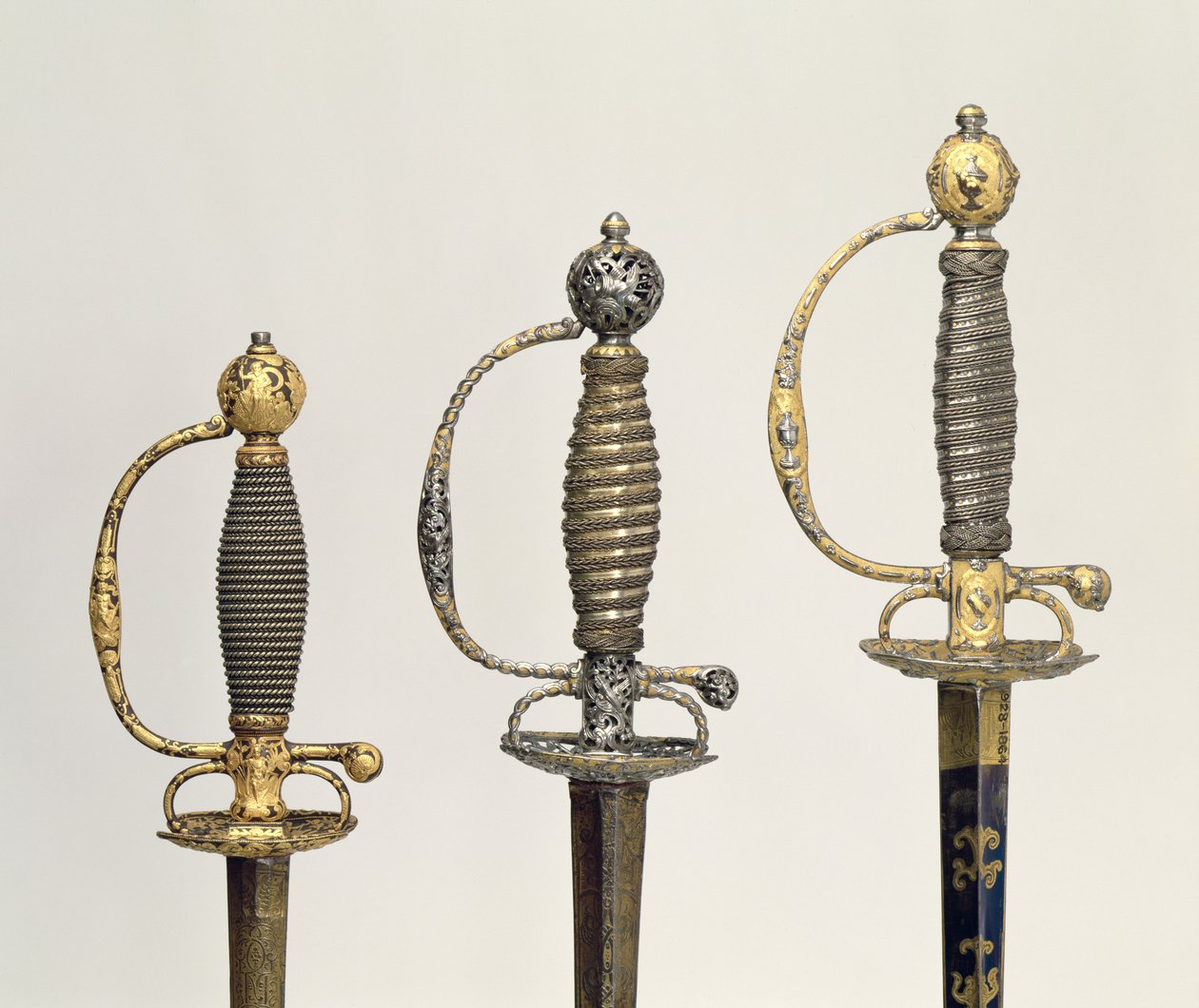 Jílec tří francouzských mečů: jeden z oceli, modřený a překrytý vzory v honěném zlatě, kolem 1730; jeden z oceli děrovaný a dlabaný a broušený z matného zlata, kolem 1760; jeden z dlátové oceli, gr od Unbekannt Unbekannt