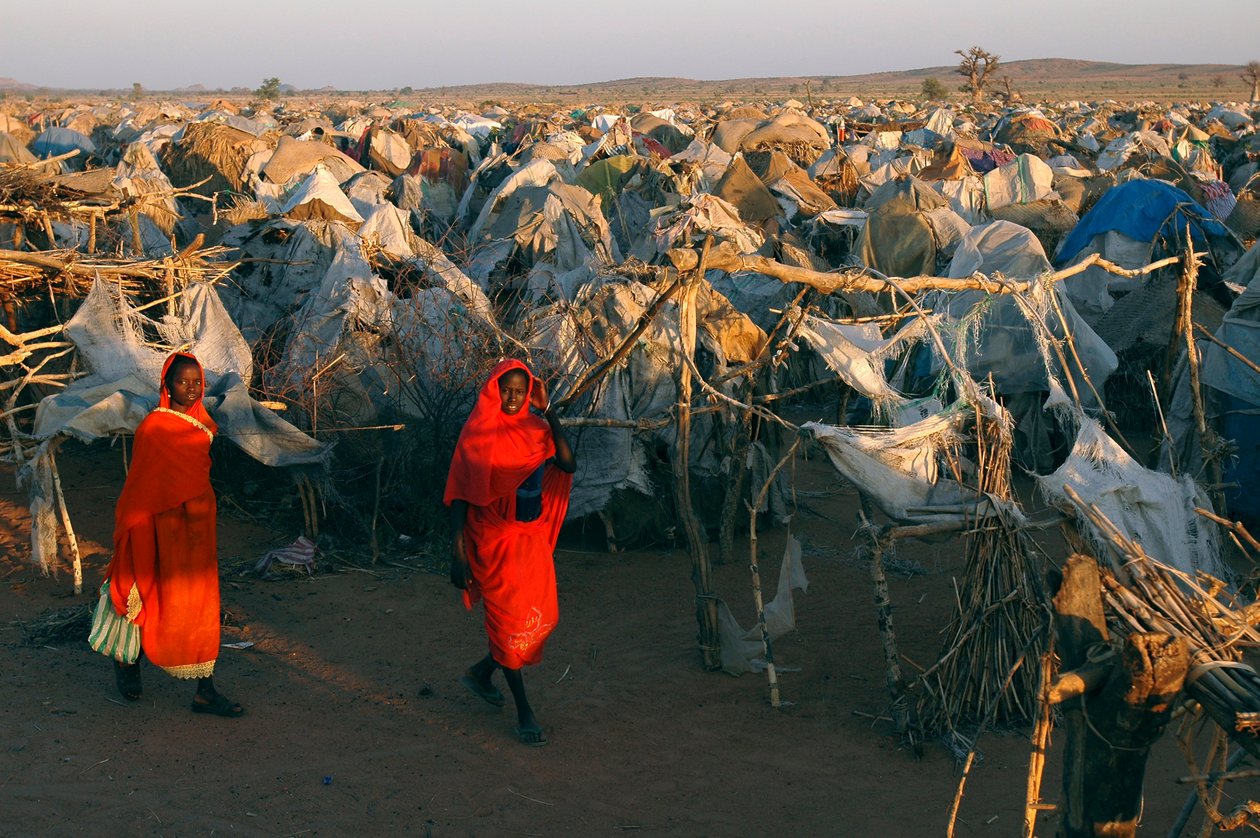 Ženy oblečené v jasně červených šatech procházejí táborem Otash pro vnitřně vysídlené osoby od Unbekannt Unbekannt