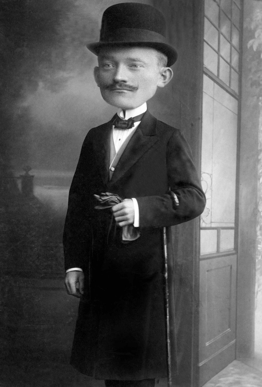 Portrét velmi elegantního muže s obří hlavou, který nosí melounový klobouk, hůl, motýlka a černý kabát. Jedná se o fotomontáž. Annees 1910 Historická fotografie, muž s obří hlavou od Unbekannter Künstler