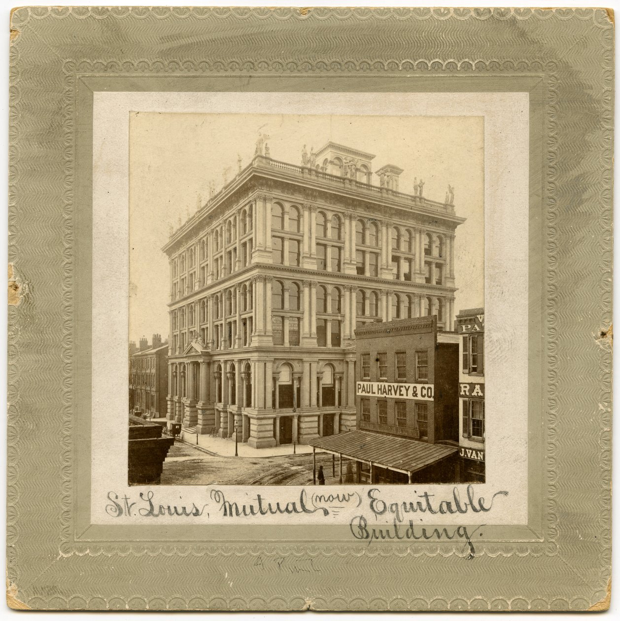 Fotografie šestipatrové budovy s postavami nahoře. Po obou stranách jsou vidět další budovy. Budova nazývaná také St. Louis Life Insurance Building od Unknown