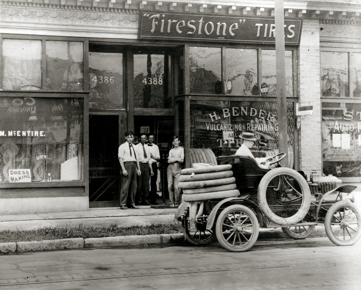 Muži a nákladní automobil na opravu pneumatik se shromáždili před prodejcem H. Bender Firestone Tire na ulici 4388 Olive Street od Unknown