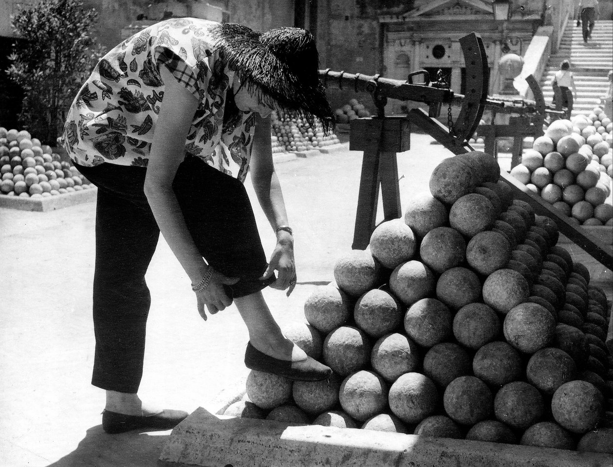 Žena si upravuje manžetu u kalhot a opírá si nohu o hromadu dělových koulí v areálu Andělského hradu v Římě. od Unknown photographer