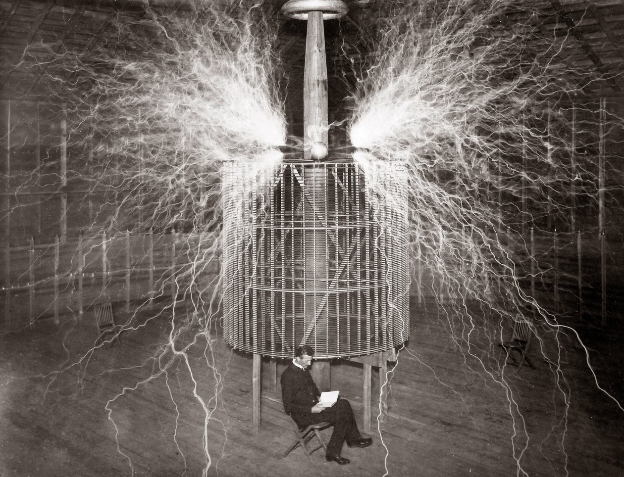 Nikola Tesla sedí ve své laboratoři v Colorado Springs se svým „zvětšovacím vysílačem“ od Unknown photographer