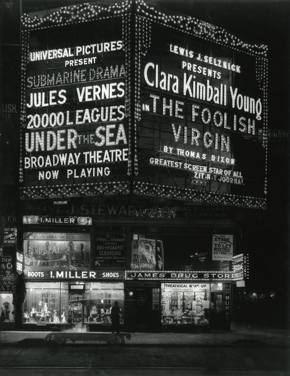 1554 Broadway na 46. ulici, I. Miller Shoes; James Drug Store a nad ním rozsvícené velké filmové stánky. od William Davis Hassler