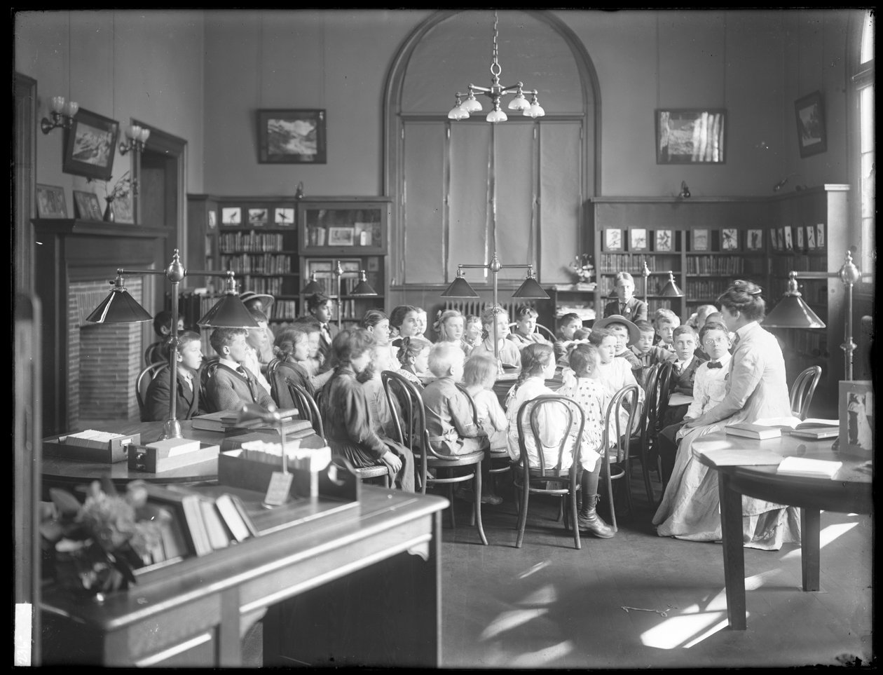 Děti poslouchají ženu v čítárně neidentifikované pobočky veřejné knihovny Queens Borough, kolem roku 1910 od William Davis Hassler