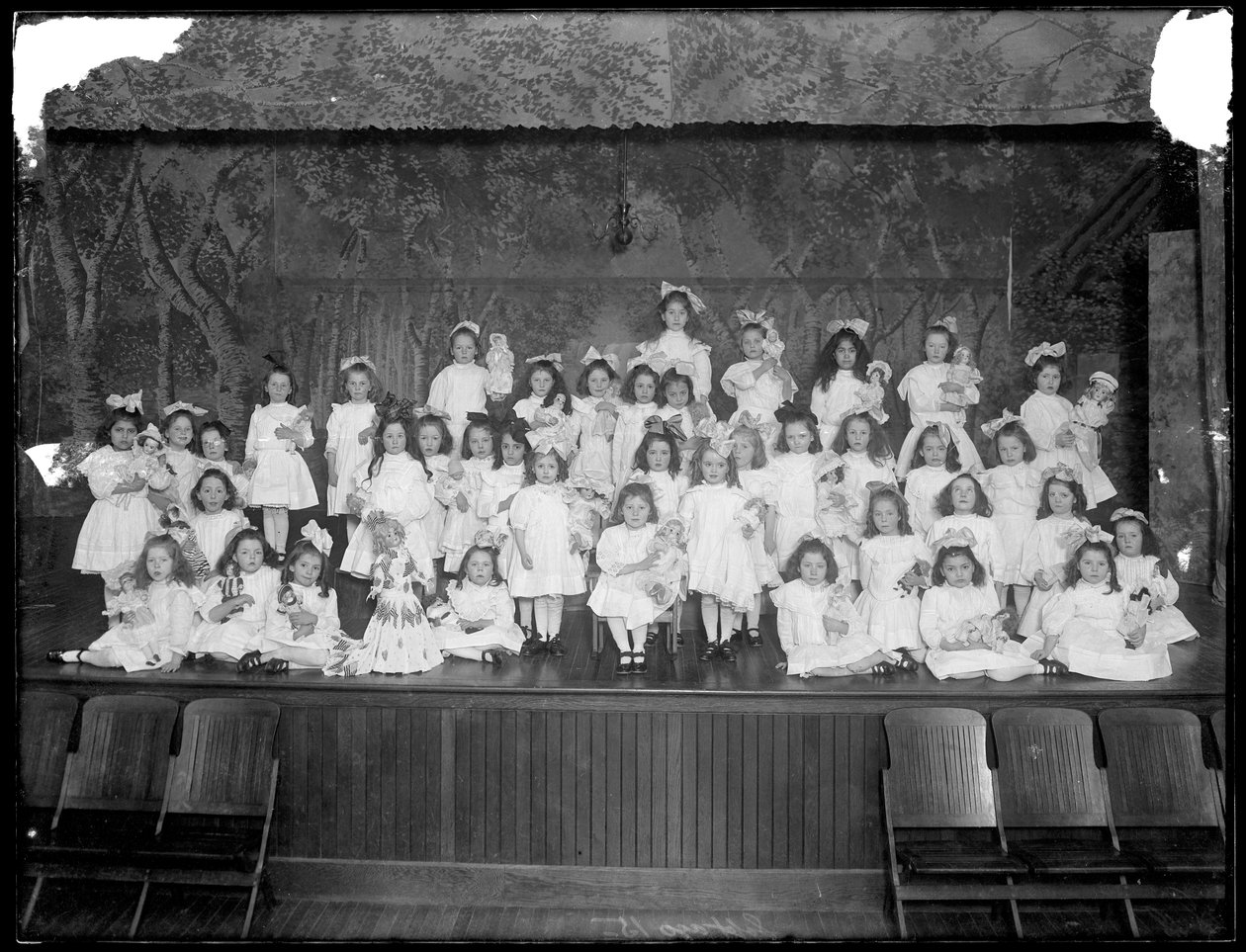 Skupina děvčátek pózujících na malém pódiu a držících panenky, pravděpodobně Roman Catholic Orphan Asylum, Kingsbridge, Bronx, asi 1911 od William Davis Hassler