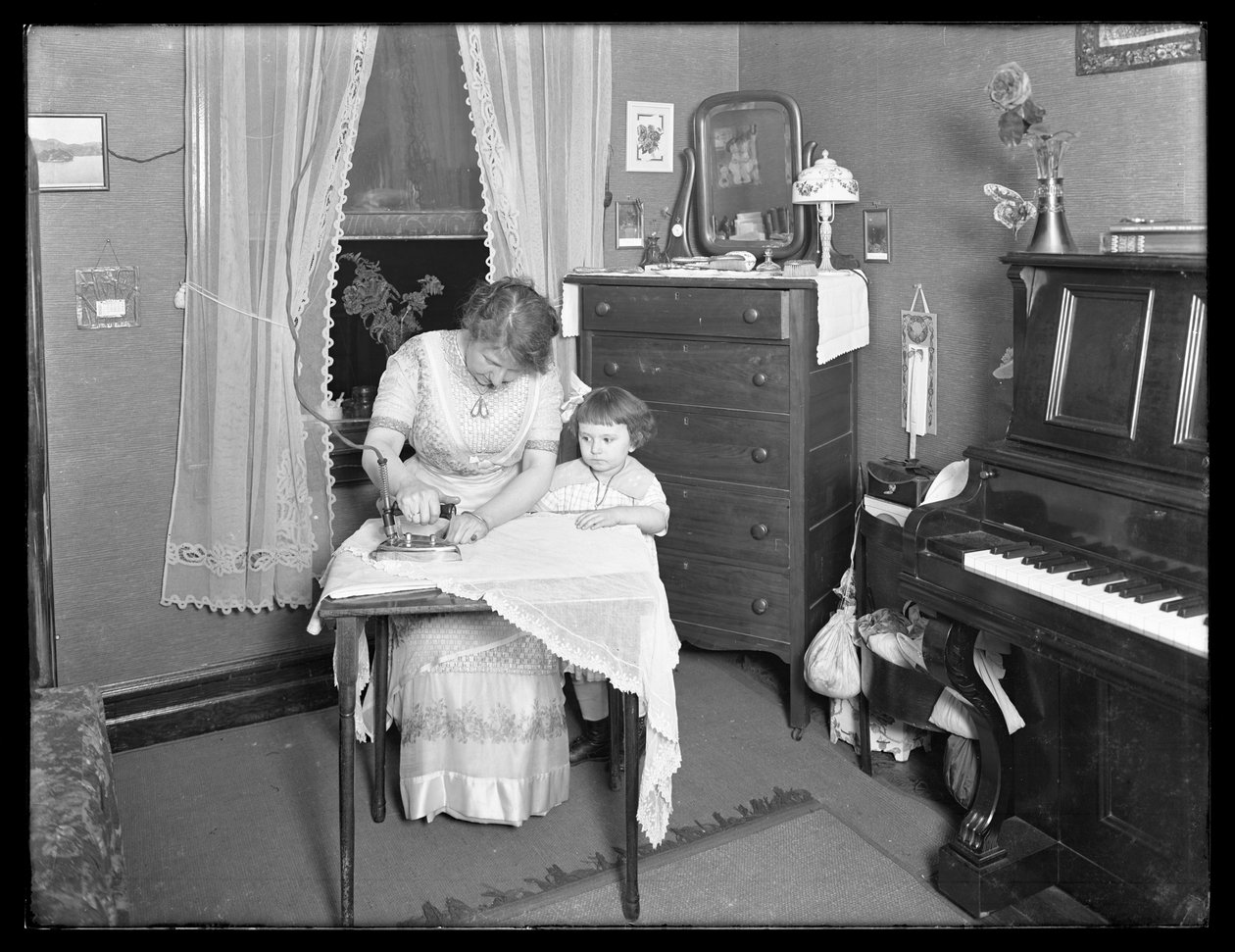 Neznámá žena předvádějící použití elektrické žehličky, sledovaná malou dívkou, cca 1913-14 od William Davis Hassler