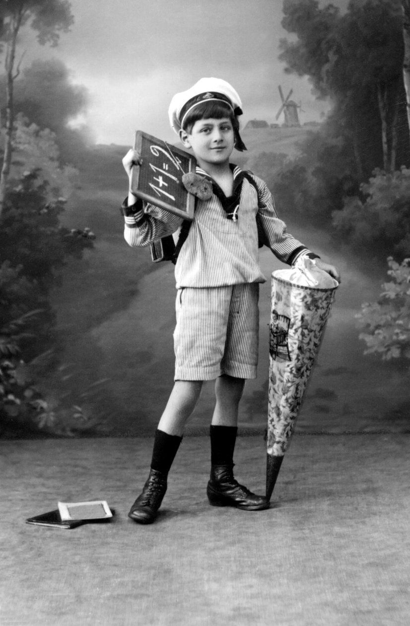 První den školy. Mladý chlapec v uniformě pózující s břidlicí znázorňující sčítání 1+1 = 2 a sáčkem s překvapením. Fotografie kolem roku 1910. od Ferdinand Georg Waldmuller