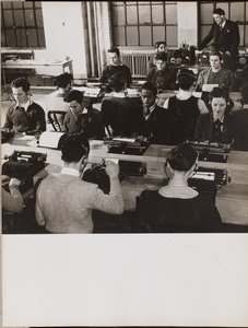 [Lidé sedí před psacími stroji a mají na uších sluchátka]