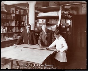 Portrét Henryho a S.G. Lindemana se svým synem nebo vnukem stojící nad dílenskými kresbami pro klavír, 1910 (stříbrný želatinový tisk)