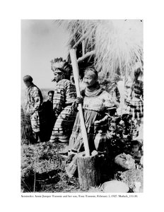 Annie Jumper Tommie pomocí hmoždíře a paličky k výrobě kukuřičné mouky a její syn Tony Tommie s čepicí z orlího peří, 5. února 1927