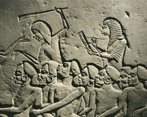 Skupina černošských vězňů obklopená strážemi ozbrojenými obušky, zatímco písař sepisuje protokol. Reliéf z Horemhebovy hrobky v Sakkáře, detail od Egyptian 18th Dynasty