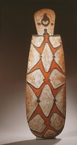 Oválný štít Asmat, vyřezávaný v reliéfu se stylizovanými postavami, maska nahoře (dřevo) od Guinean New