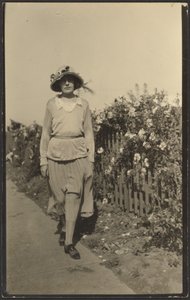 [Žena kráčející podél plotu s květinami] od Louis Fleckenstein