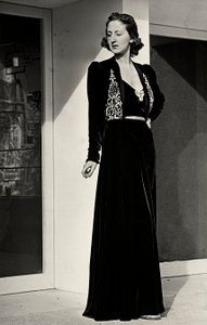 Modelka má na sobě dlouhé večerní šaty z tmavého sametu s vyšívaným zdobením, které vytvořil italský couture house "Fercioni". (černobílá fotografie)