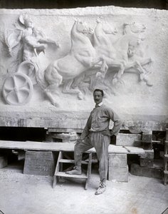 Celovečerní portrét slavného sochaře Pietra Canonica. Pózuje ve svém ateliéru před mramorovým vysokým reliéfem, na kterém pracuje (černobílá fotografie)