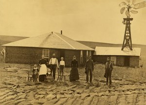 Rodina usedlíků, mimo jejich drnový dům s větrným mlýnem na střeše přilehlé budovy v Custer County, Nebraska, cca 1885 (č/b foto) od Solomon D. Butcher