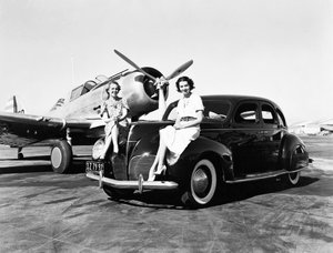 Kalifornie: 1939 Dvě ženy sedí na blatnících sedanu Lincoln Zephyr z roku 1939 na letišti s jednomotorovým letadlem zaparkovaným za nimi (černobílá fotografie) od Unbekannt