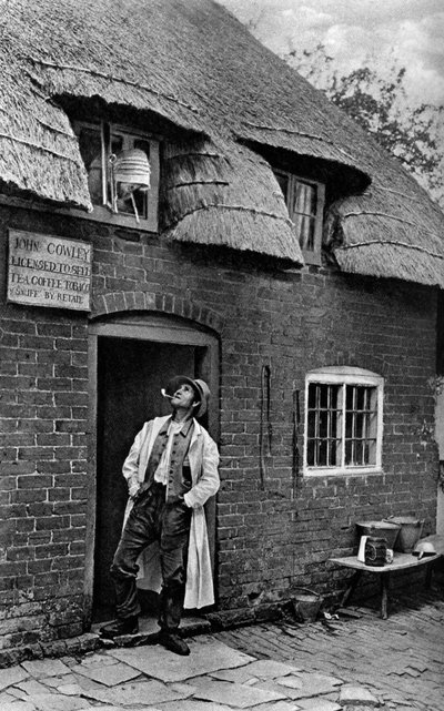 Muž kouří dýmku před obchodem, Worcestershire, c1922. od A. W. Cutler
