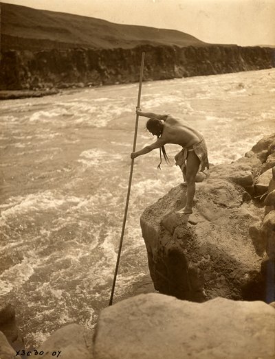 Indián Tlakluit stojící na skále a lovící ryby s namáčecí sítí, asi 1910 (čb fotografie) od Edward Sheriff Curtis