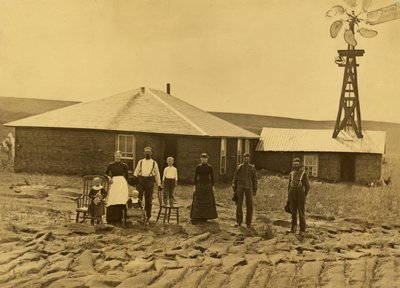 Rodina usedlíků, mimo jejich drnový dům s větrným mlýnem na střeše přilehlé budovy v Custer County, Nebraska, cca 1885 (č/b foto) od Solomon D. Butcher